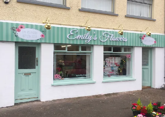 Emily's Flowers shop front with a mint green illuminated fascia and hanging lights, viewed along the pavement.