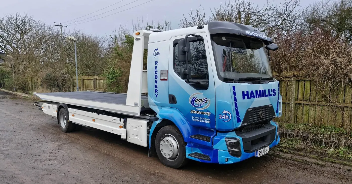 Hamill Group flatbed recovery truck in a blue geometric vinyl wrap, parked on a rural road.