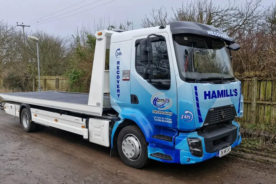 Hamill Group flatbed recovery truck in a blue geometric vinyl wrap, parked on a rural road.