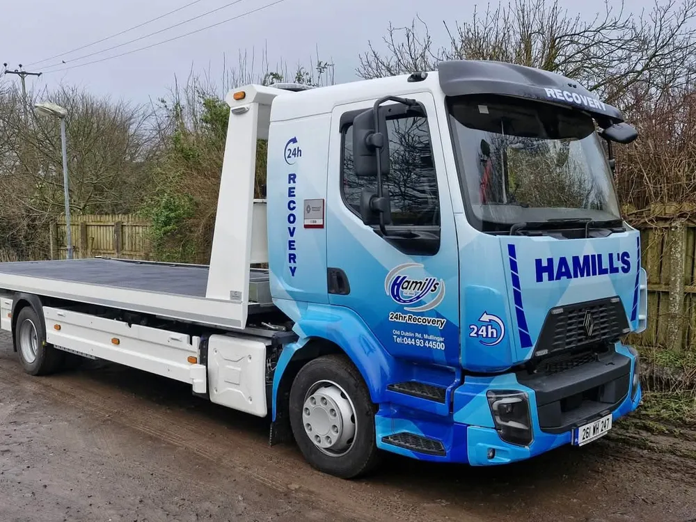 Hamill's 24hr Recovery flatbed truck in a blue geometric vinyl wrap, parked on a rural road.