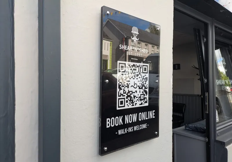 Shear 'n' Shed black acrylic plaque with QR code, Book Now Online and Walk-ins Welcome, fixed with standoffs beside a doorway.